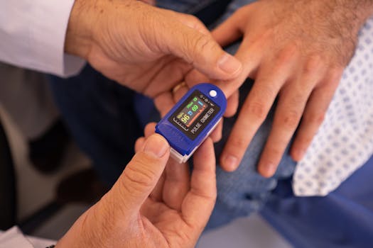 Close-up of a doctor's hand using a pulse oximeter on a patient's finger in a hospital setting.